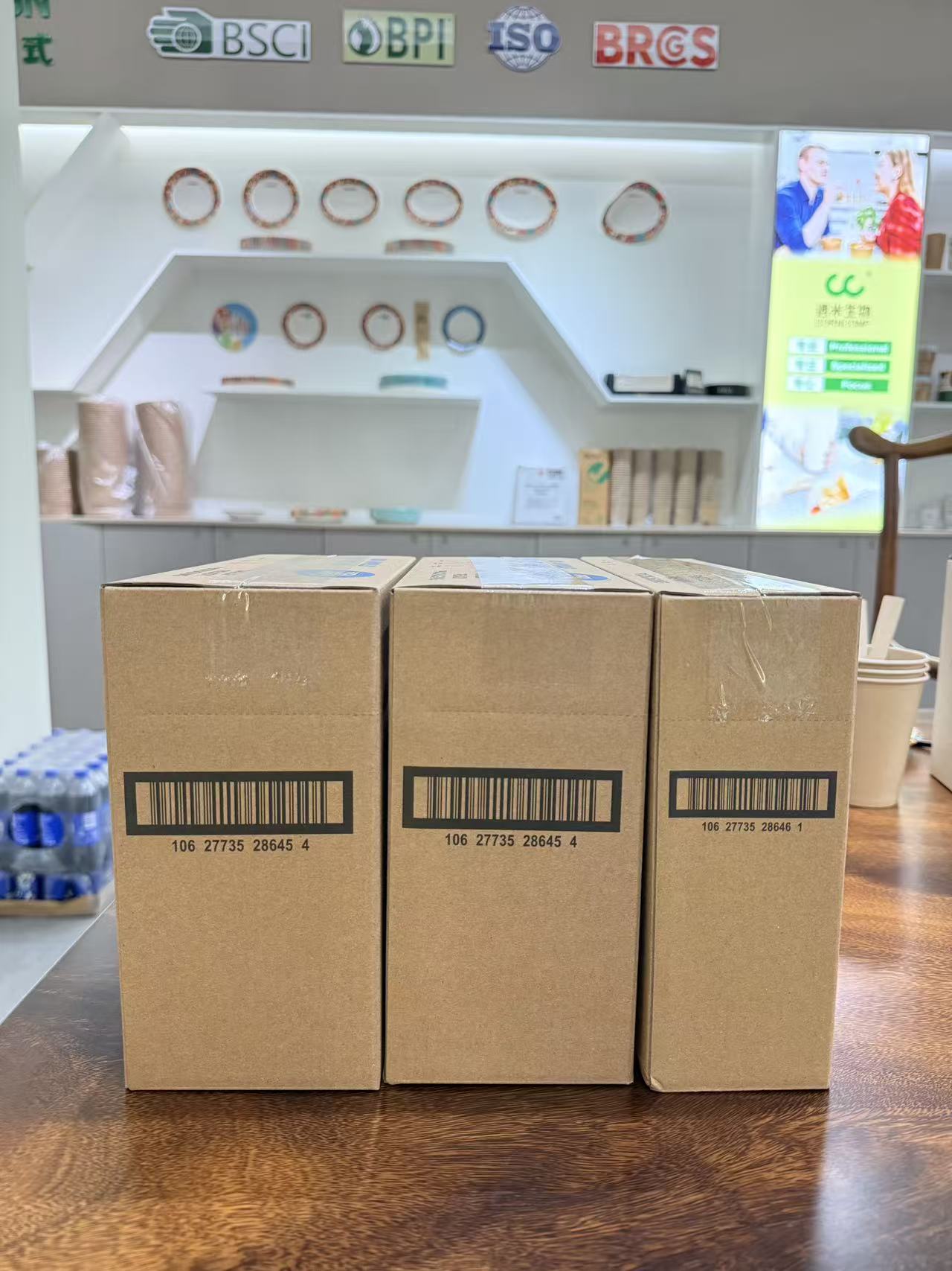 Sealed Great Value paper straw export cartons at Corncomp's showroom, with BSCI, BPI, ISO and BRCGS certification badges in the background